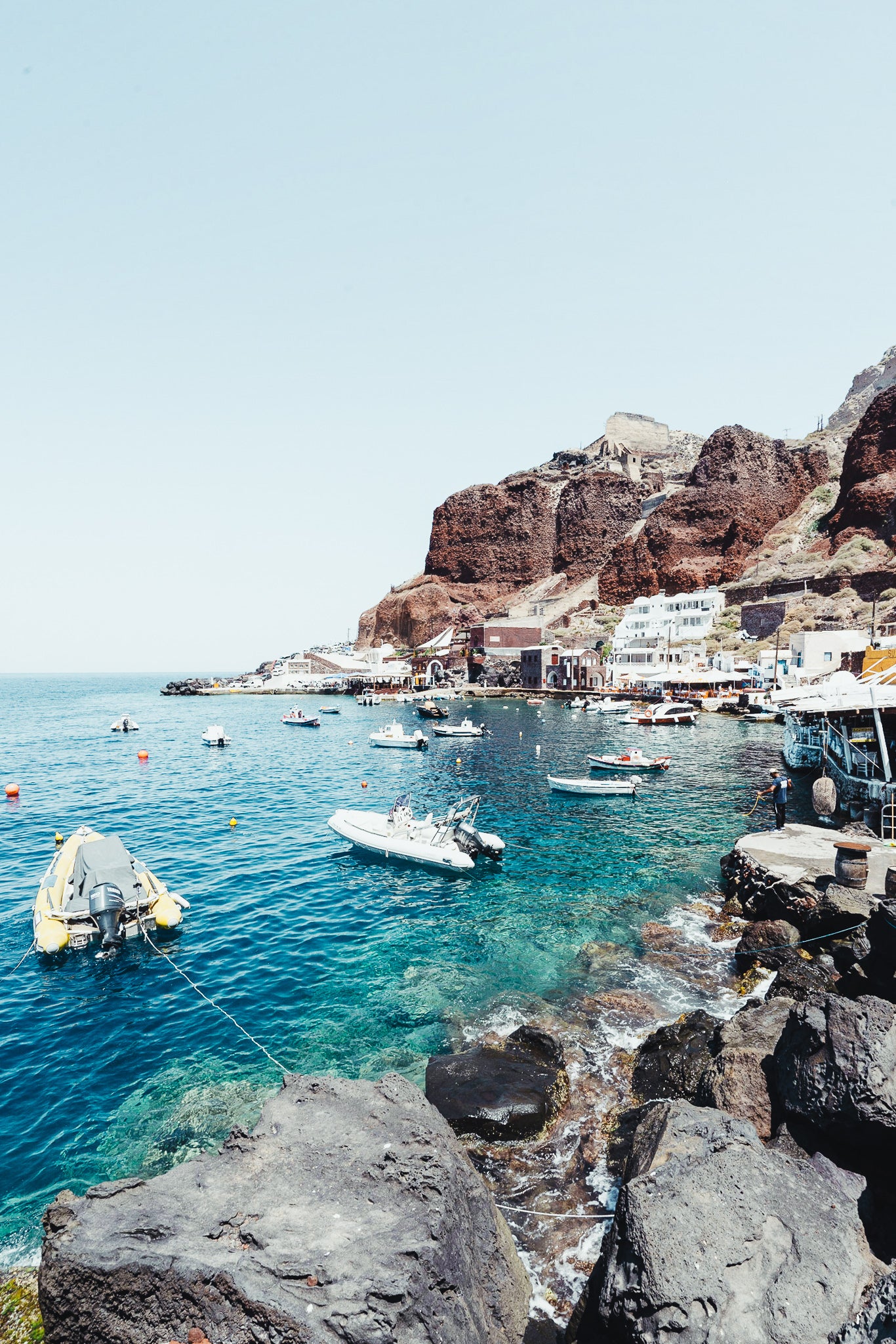 The bay and port of Amoudi is located on the northwestern tip of the island of Santorini, on the seafront below the town of Oia. The white buildings of the Amoudi town built into the blood-red slope of the caldera cliff look very picturesque.